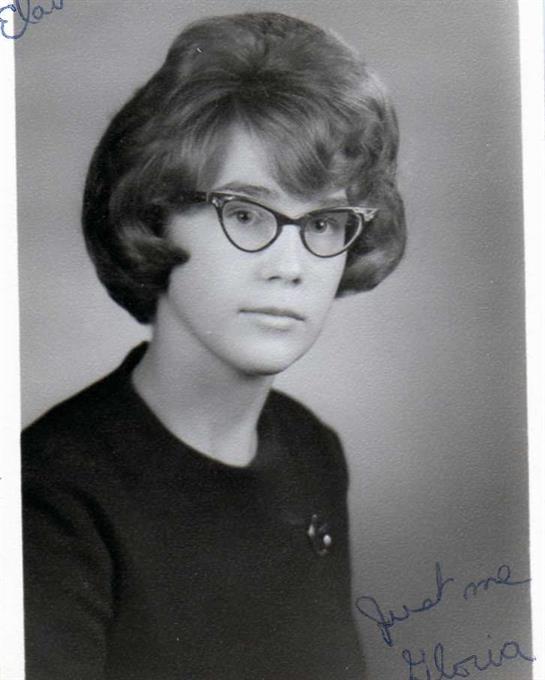 A young woman poses for a formal portrait, wearing glasses and a dark outfit typical of the 1960s.
