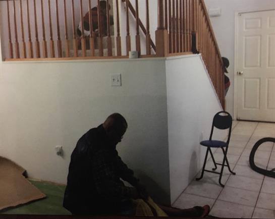 A person is seated against a wall with their head down, while another figure is upstairs.