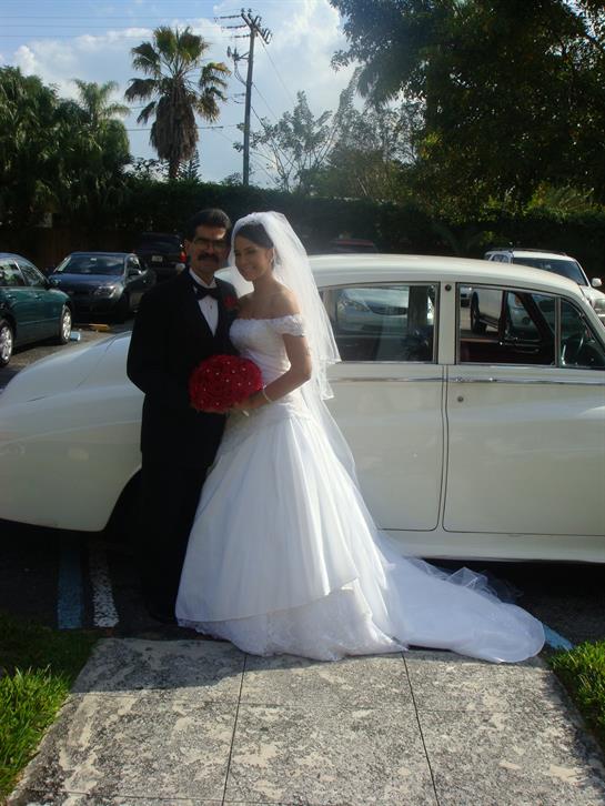 A happy couple in wedding attire poses with a vintage car, celebrating their special moment.