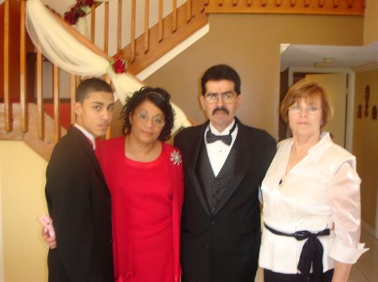 Four adults dressed in formal clothing pose together, surrounded by festive decorations in a home.