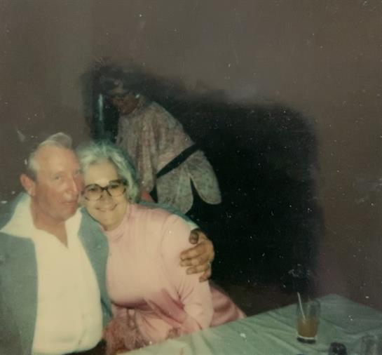 An elderly couple shares a warm moment at a lively gathering with friends in a cozy setting.