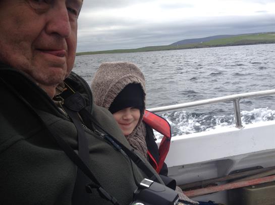 A man and a child wearing warm clothes sit together on a boat, enjoying the water view.