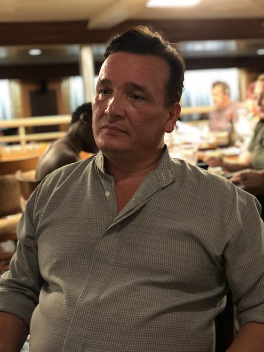 A man at a restaurant table chats with fellow diners enjoying their meals.