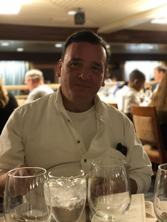 A man sits at a dining table with drinks, enjoying a lively dinner with friends in a restaurant.