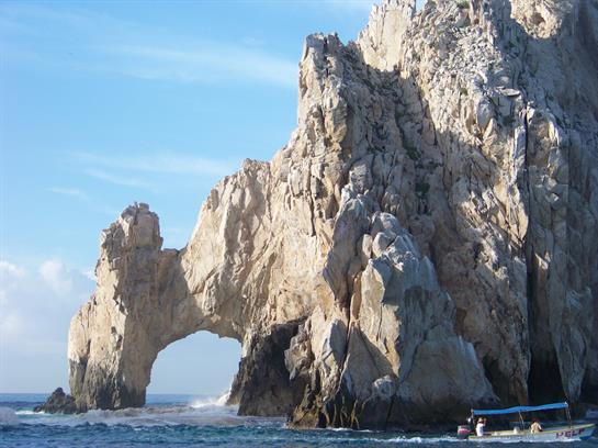 Visitors admire a stunning natural rock arch against the clear blue sky and ocean at Cabo San Lucas.