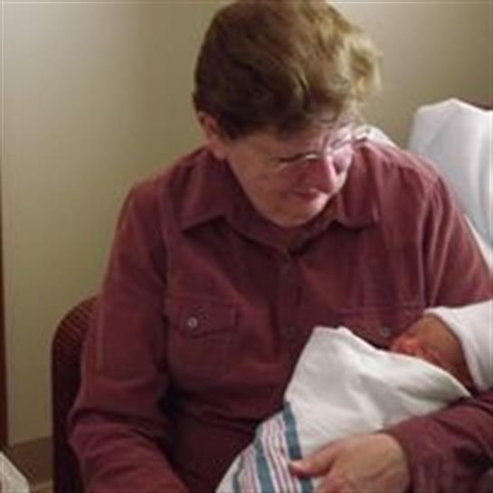 Grandmother gently cradles her newborn grandchild in a hospital room, filled with love.