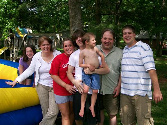 A joyful family poses together in a backyard with children enjoying a bouncy castle.