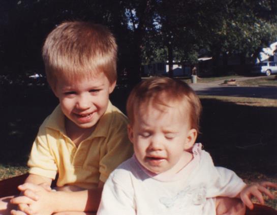 Two kids smile in a park under the warm sun, capturing a playful and carefree summer moment.