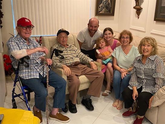Six family members and a child gather on a couch, sharing smiles and stories in a warm atmosphere.