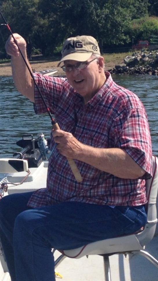 An older man happily catches a fish while fishing on a boat in a serene lake.