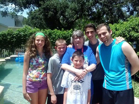 A group of six people gathers by a pool, smiling and enjoying a warm summer day together.