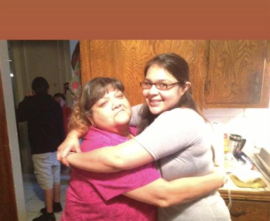 Two women smile and hug each other tightly while enjoying family moments in the kitchen.