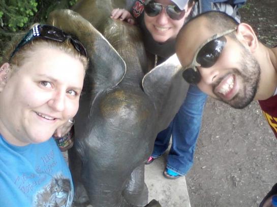Friends gather around a life-sized bronze elephant statue, smiling under the bright sun.