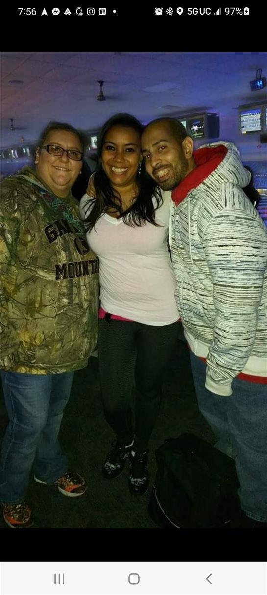 Three friends pose together smiling at a lively outdoor event during the evening.