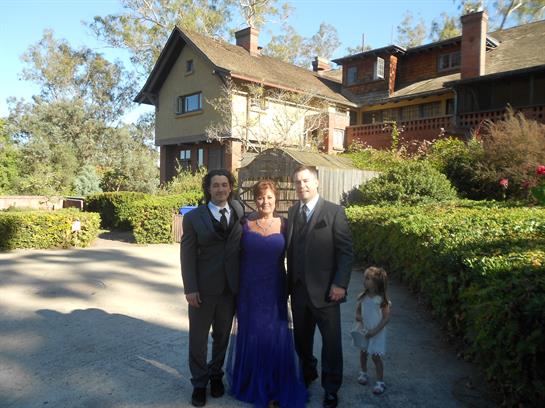 Three adults dressed in formal wear stand together with a child in a casual outfit outside a house.