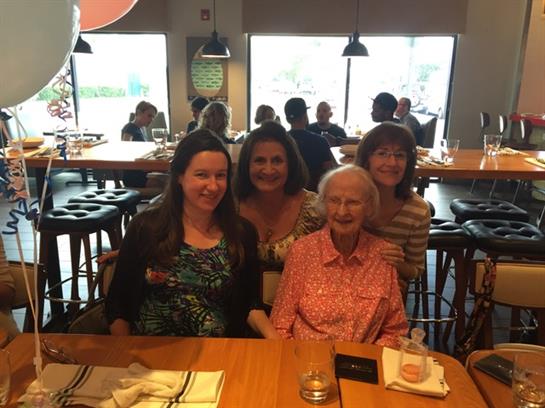Four generations enjoy a pleasant lunch together in a bustling restaurant atmosphere.
