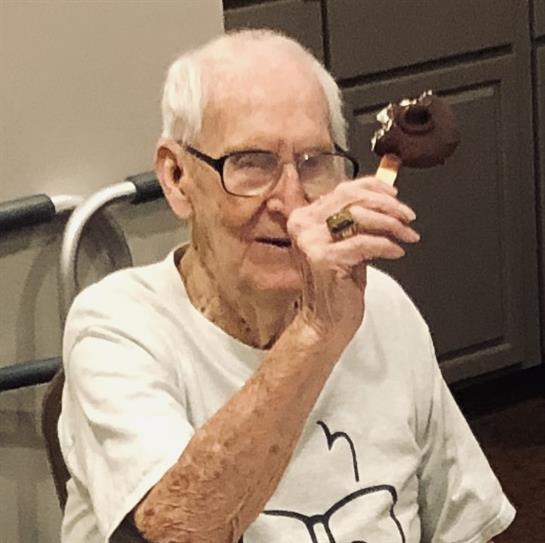 An elderly man with glasses enjoys a chocolate treat while seated in a cozy, modern room.