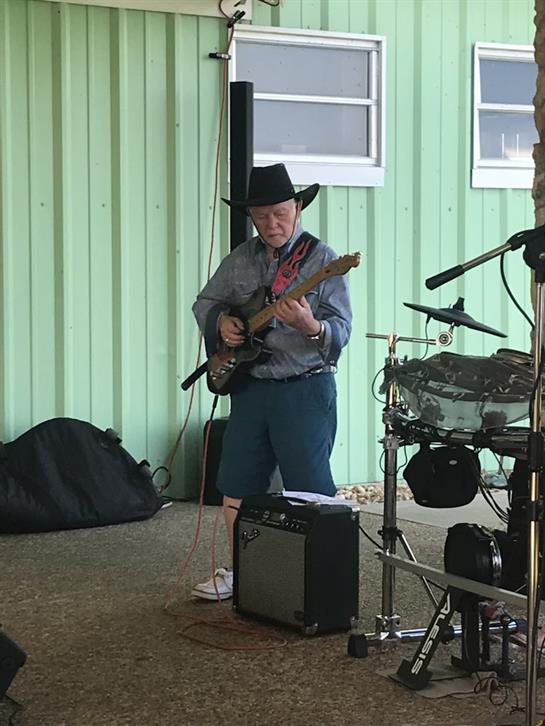Elderly musician showcases skill on electric guitar during outdoor country music performance.