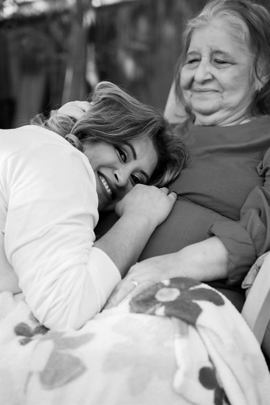 A joyful woman leans against an elderly woman, both sharing a loving moment together.