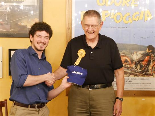 A proud winner shakes hands with an older man, holding a blue cap to celebrate a victory.