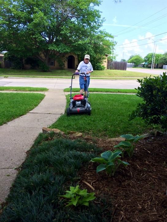 Individual mows the lawn in a residential area while enjoying a warm and sunny afternoon.