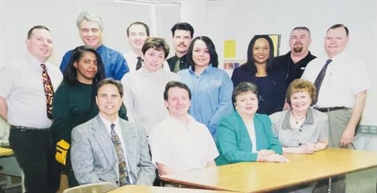 A diverse group of professionals poses for a photo in a bright office meeting room.