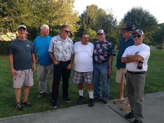 A group of eight friends pose together, smiling and enjoying a relaxed moment in a park setting.