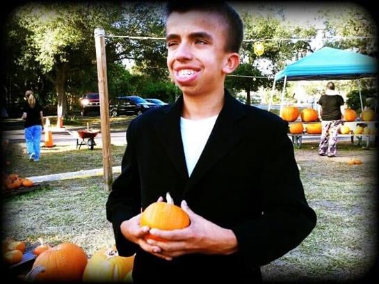 A person stands happily holding a pumpkin amidst festive decorations and autumn scenery.