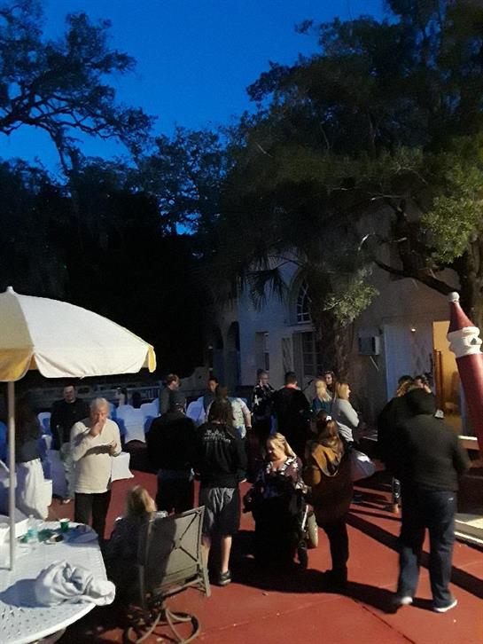 Many guests are enjoying a lively outdoor gathering during the evening at a beautiful venue.