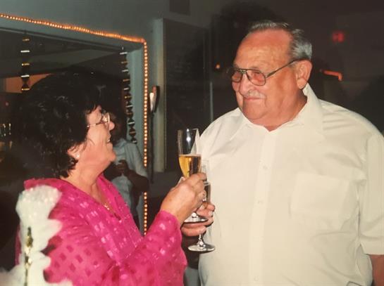 Two seniors toast with drinks, smiling warmly during a joyful celebration in a lively setting.