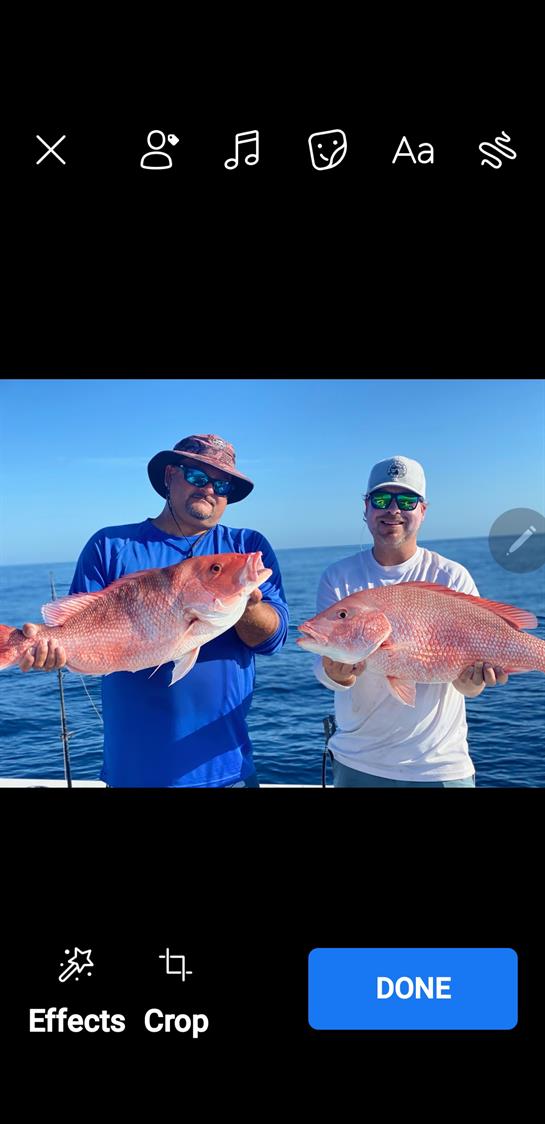Two fishermen proudly hold their large catches of red snapper on a sunny day at sea.