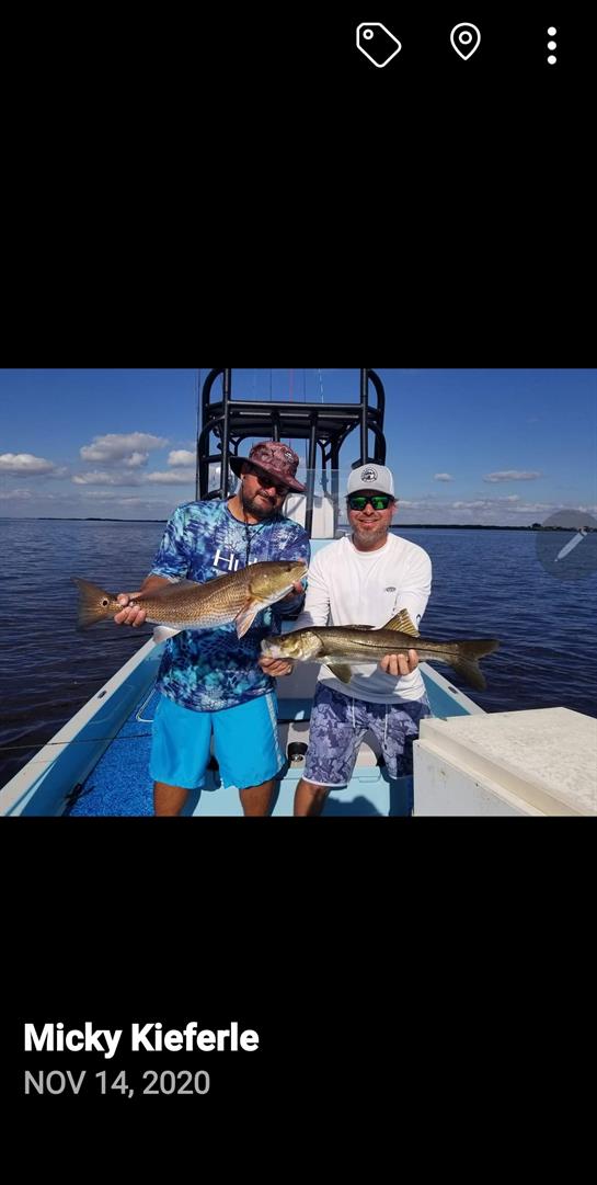 Two fishermen proudly hold their large catches while enjoying a sunny day on the water.