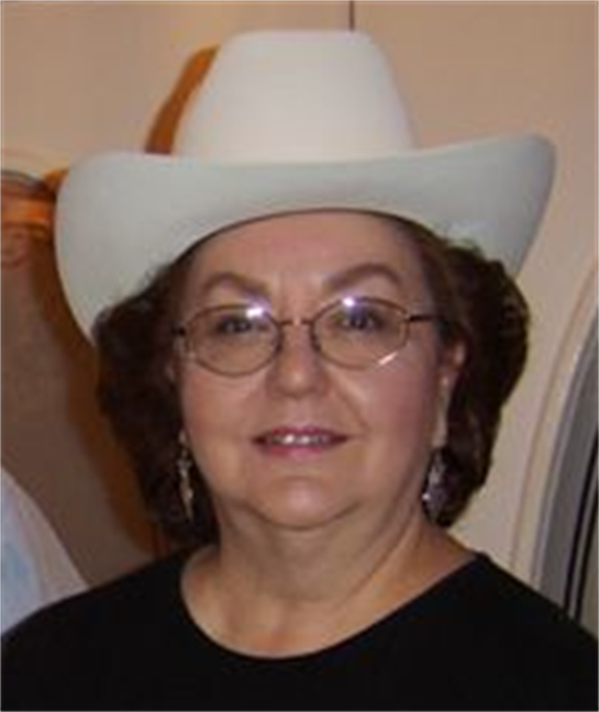 A woman in glasses and curls smiles in a white cowboy hat at a social event.