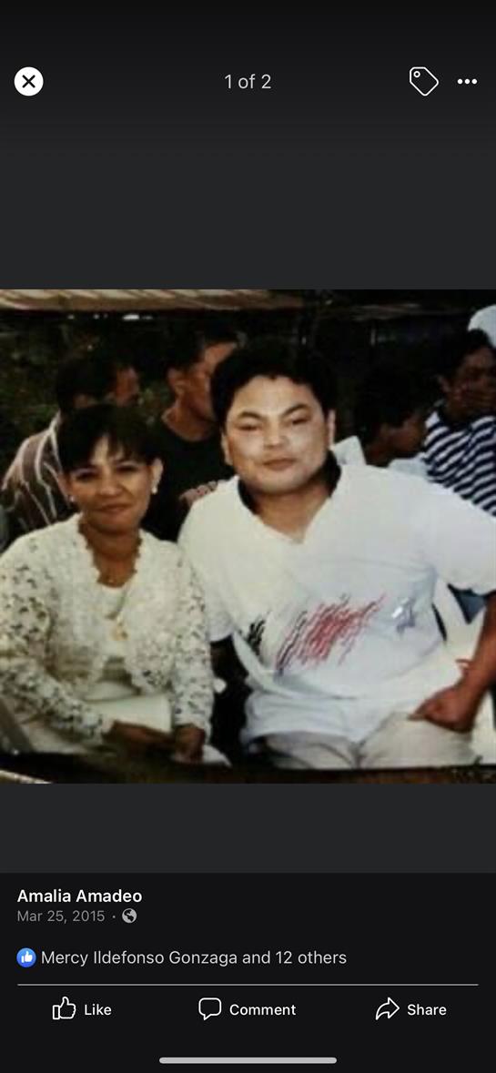 Two friends smile together while sitting among a cheerful group, enjoying their time outdoors.