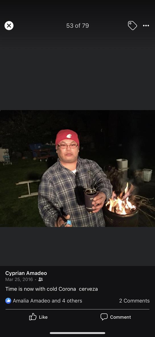 A man by a fire pit at night holds a drink and gazes confidently at the camera.