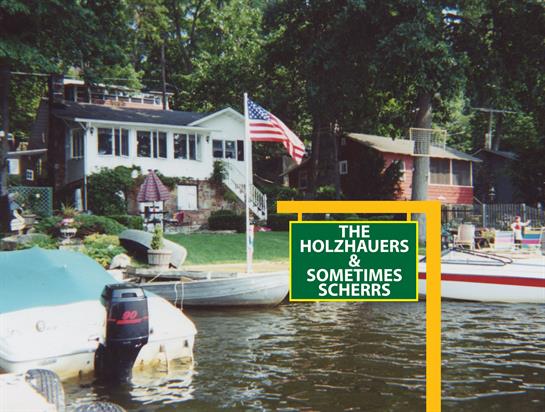 A sign indicates family names by the lakeside, showcasing boats and a relaxing natural setting.