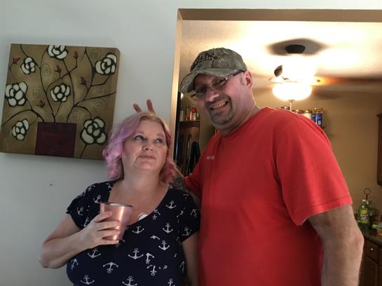 Two friends share a lighthearted moment while holding drinks during a lively home gathering.