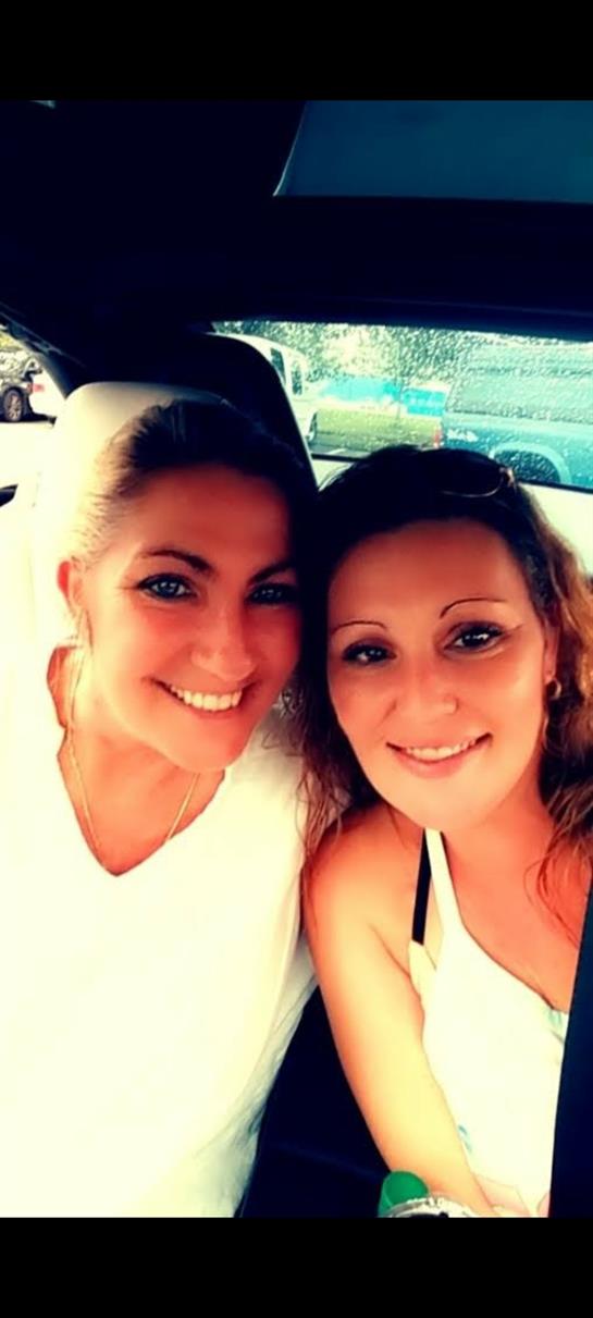 Two smiling women pose for a selfie inside a car on a bright day, capturing a joyful moment.