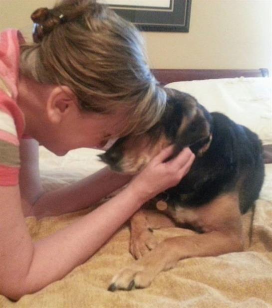 A woman gently interacts with her dog, showing love and affection in a cozy bedroom setting.