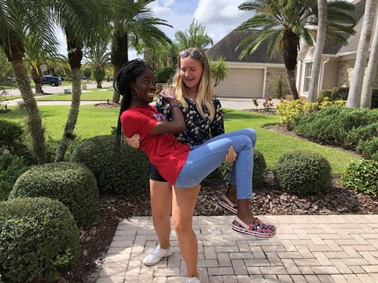 Two friends share a joyful moment outside a house, with one lifting the other in playful cheer.