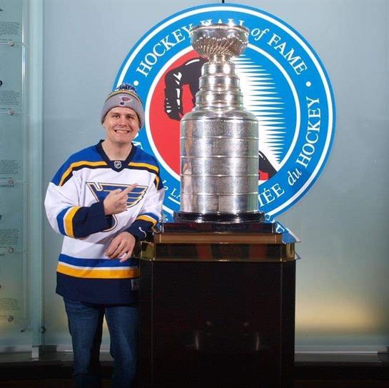 Visitor shows excitement while standing next to the championship trophy at a hockey hall of fame.