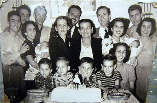 A large family gathers around a decorated cake, smiling and celebrating a special occasion.