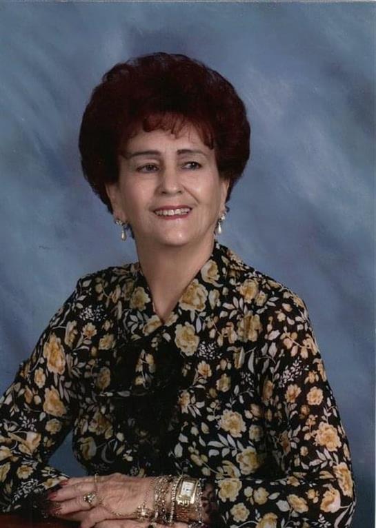 A woman with curly hair is smiling while sitting for a formal portrait wearing a floral blouse.