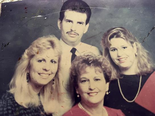 Four family members pose closely together, smiling warmly in a vintage setting from the 1980s.