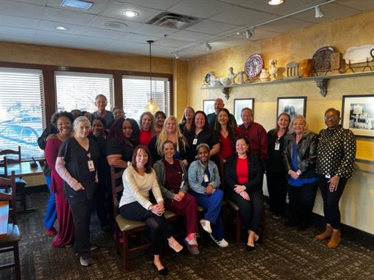 Numerous employees pose together in a well-lit restaurant, smiling and enjoying their time.