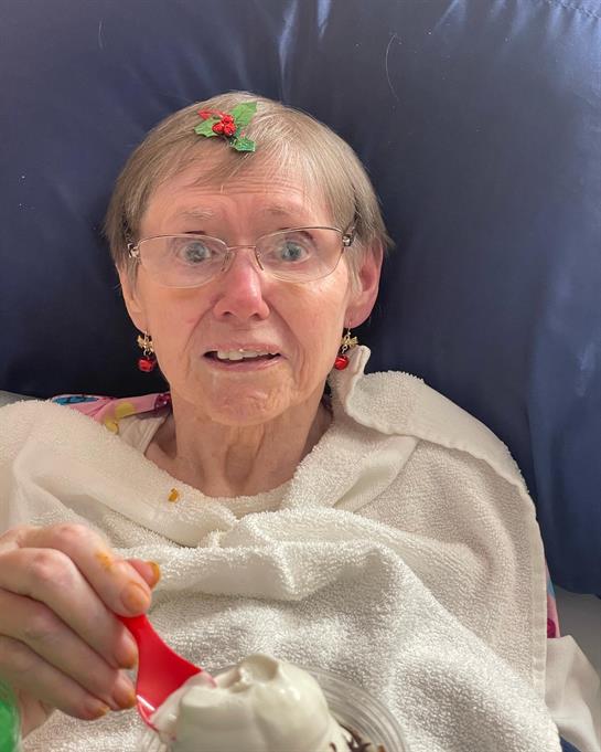 An elderly woman beams as she holds a festively decorated spoon in a casual setting.
