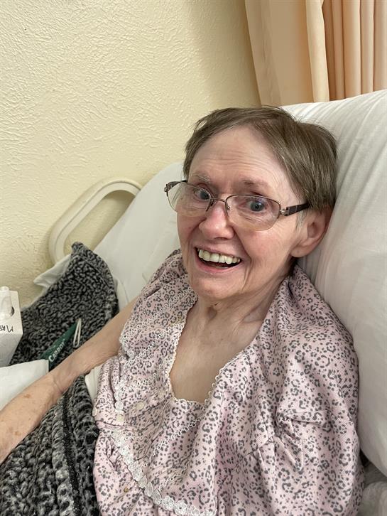 Elderly woman with a joyful expression sits comfortably in her room during late afternoon.