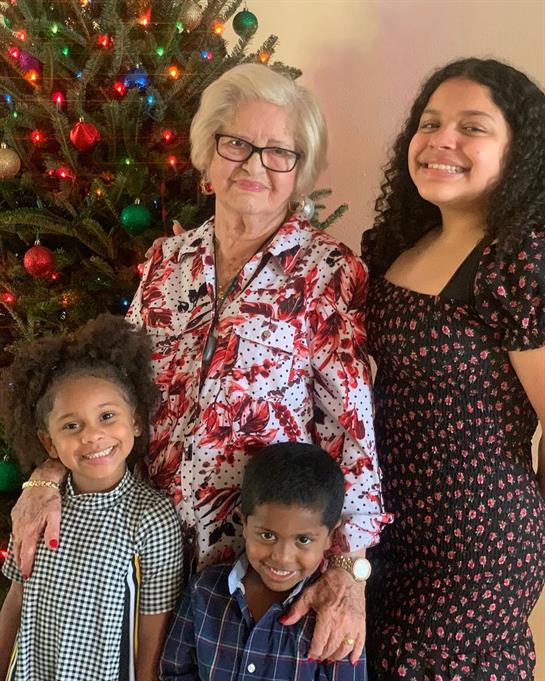 A joyful family stands together by a colorful Christmas tree during a festive celebration.