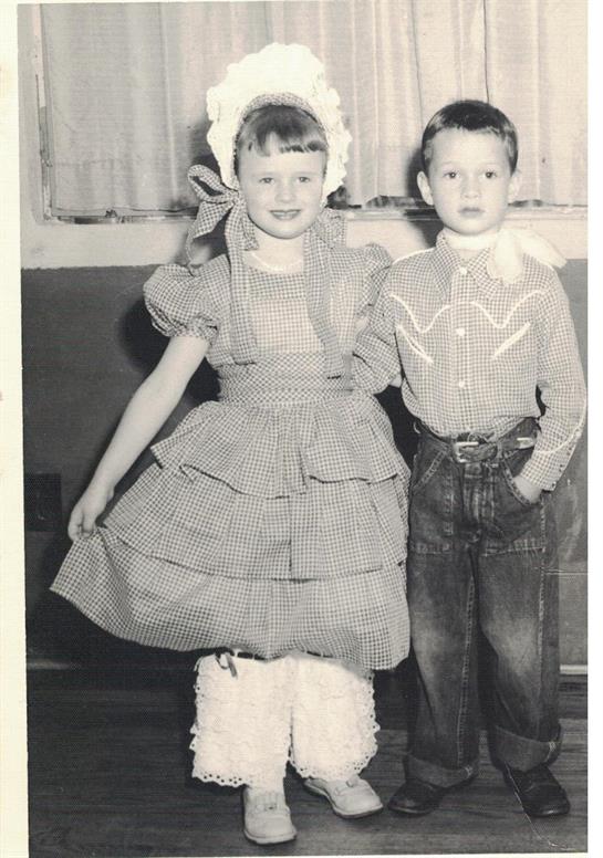 Two kids in traditional outfits smile at a lively community center event.