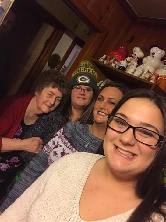 Four women smile happily together in a cozy setting, surrounded by decorations and memories.